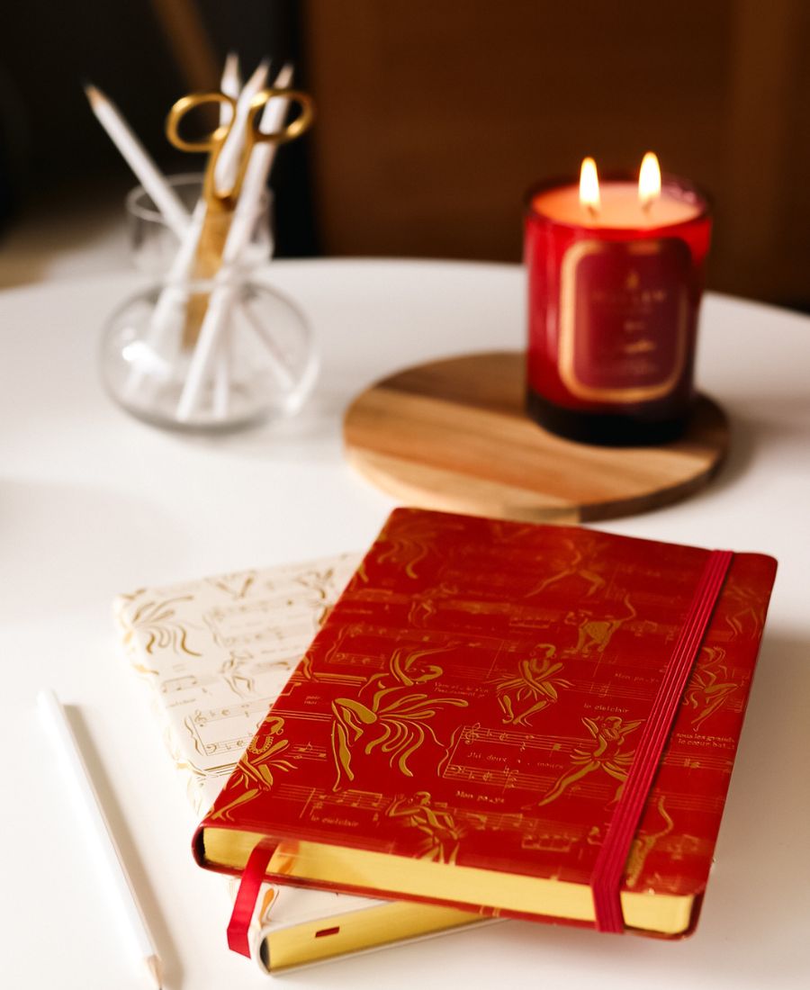 This is a lifestyle image of our Ode to Josephine journals in red and cream with gold design.  There is an image of our Josephine candle burning in the background.