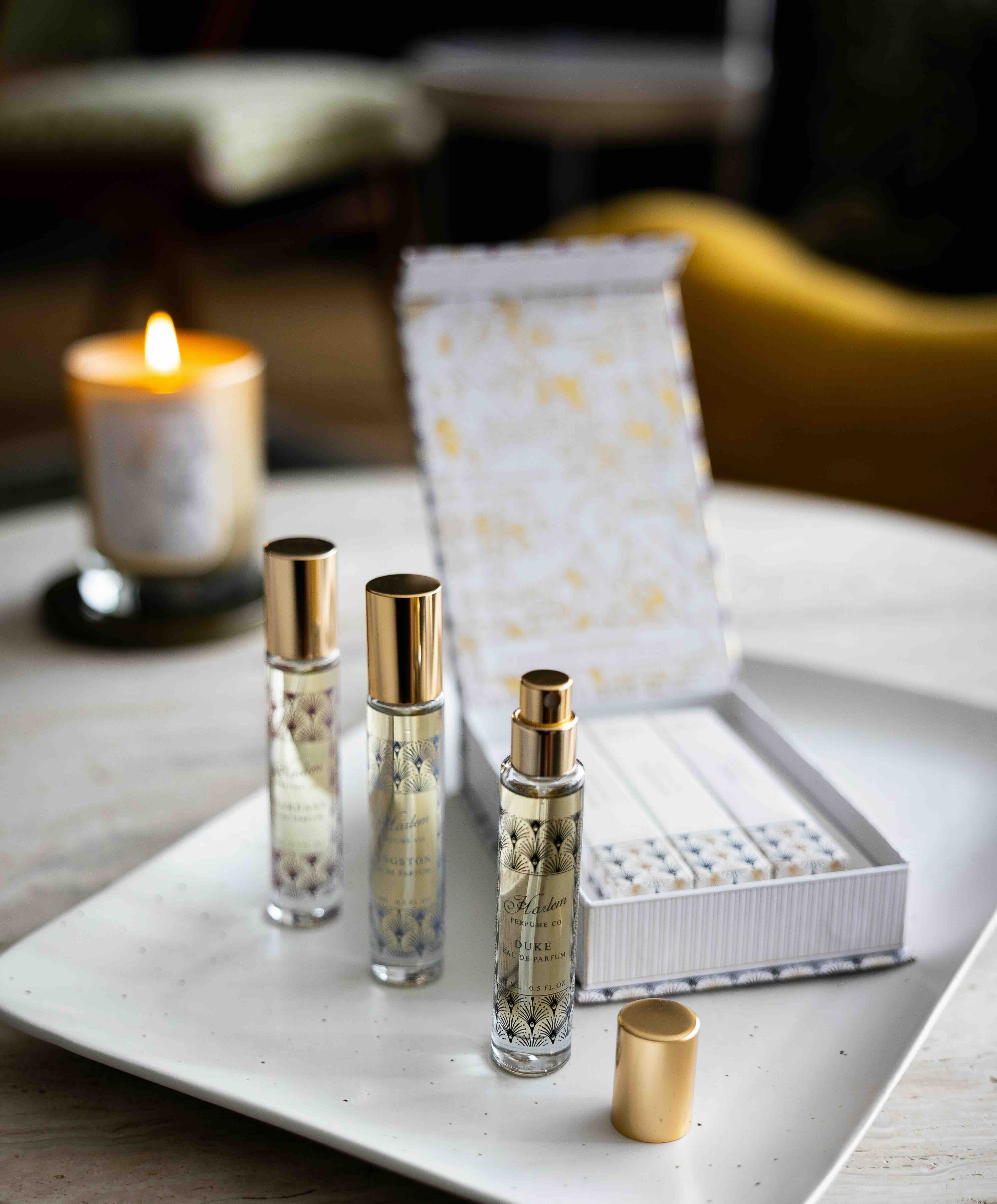 This is a lifestyle image of the perfume discovery box that contains the Langston, Duke and Speakeasy fragrances.  There is a candle burning in the background.