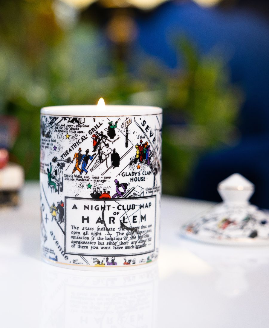 This is a lifestyle image of our night club map of Harlem candle in black-and-white with pops of color. This candle has a dome lid and is Fragrance with the Langston scent. In this image, the lid is positioned next to the candle 